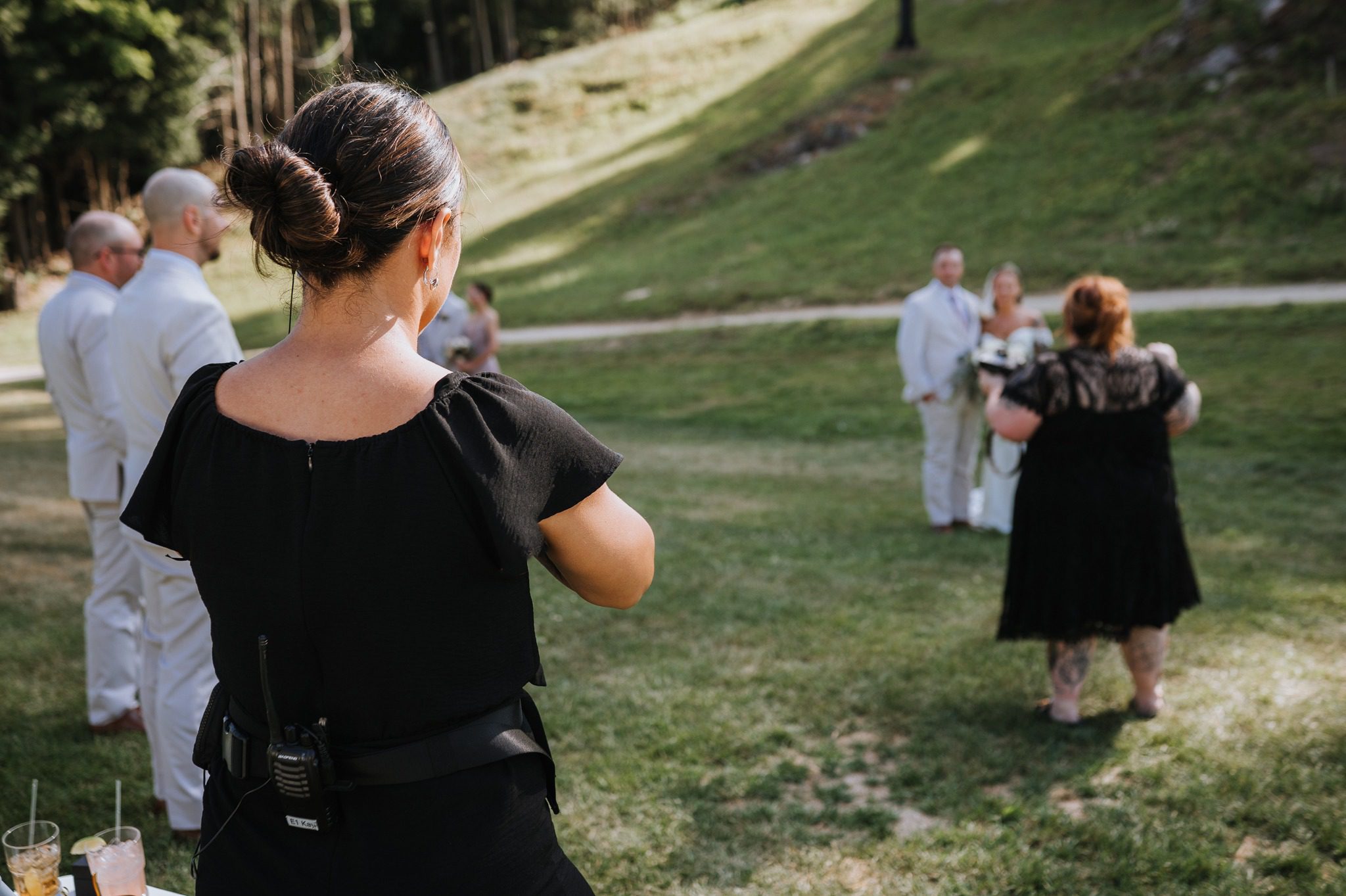 Kayla wearing a radio while watching wedding photographs being taken outdoors at Lost Valley